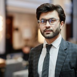 Waist up portrait of successful Middle-Eastern businessman looking at camera while standing in hotel lobby, copy space